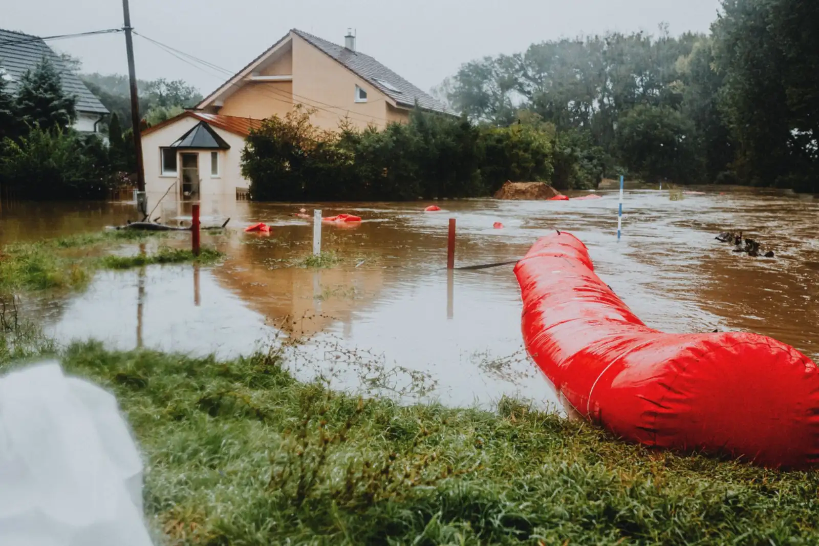 Maison et jardin sous l'eau après un orage, une barrière anti-crue rouge posée au bord : le moment où la cave se remplit et où il faut une pompe vide-cave